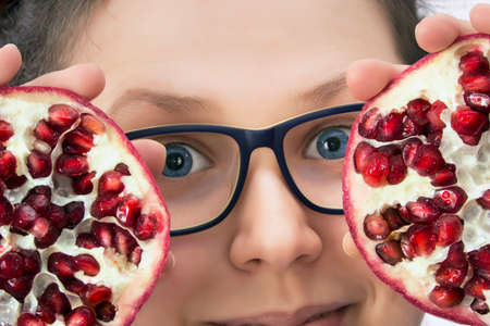 Close view of a smiling young woman with an eyeglasses and a pomegranate in a white backgroundの写真素材