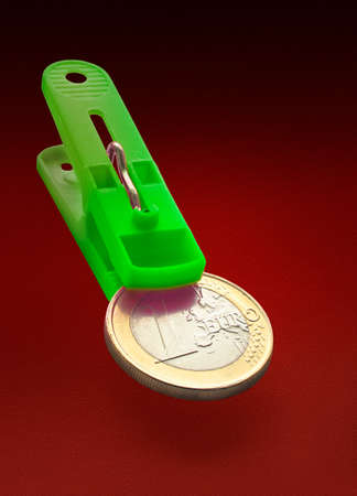Close view of one euro coin in green clothespin maw in a red gradient backgroundの写真素材