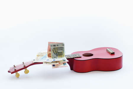 Close view of small guitar ukulele and euro banknotes in a white background