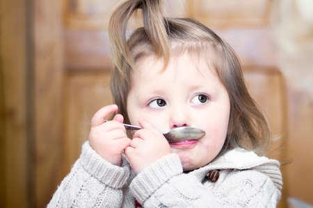 Portrait of a little girl with a spoon in the mouthの写真素材