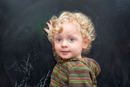 Little boy with curly hair at the old black school boardの写真素材