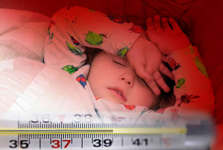 Mercury thermometer showing high temperature and a little sick girl in bedの写真素材