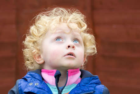 Little boy with golden curly hair looking at the sky in a red backgroundの写真素材