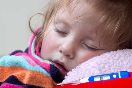 Electronic thermometer showing  temperature and a little sick girl in bedの写真素材