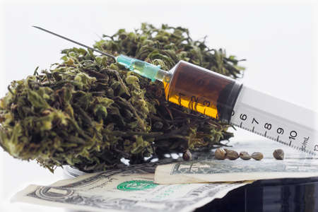 Syringe with brown liquid and hemp seeds and dried hemp leaves on dollar banknotesの写真素材