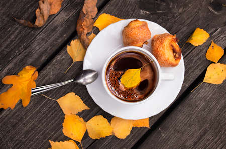 Coffee mug and a cake in the middle of yellow autumn leaves on a retro wooden tableの写真素材