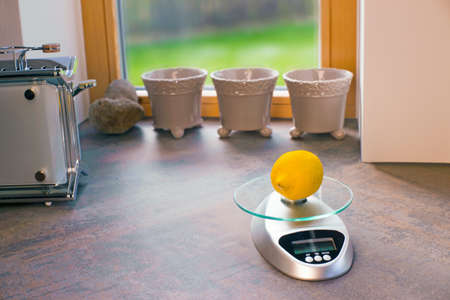 Lemon on an electronic scales on a kitchen tableの写真素材