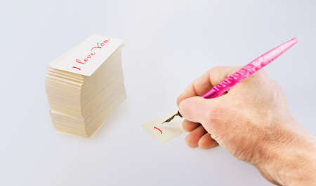 Man's hand with an old pen and white paper cards with inscription I LOVE YOU on a gradient...