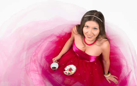 Cheerful young female smiling and holding a cup of coffee in a white backgroundの写真素材