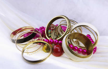 Close view of golden bracelets and beads on a white clothの写真素材