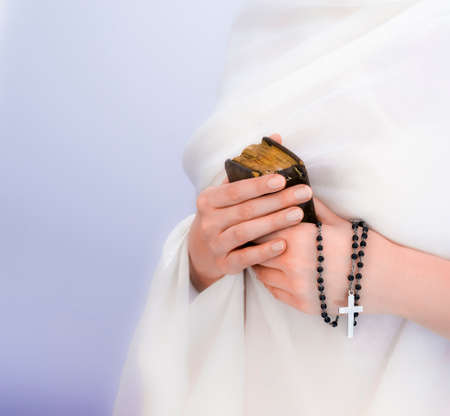 Young woman's hands with a rosary, bible and a white clothing in a backgroundの写真素材