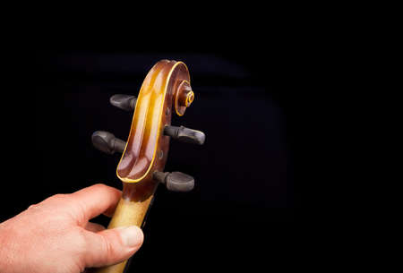 Men's hand on violin's fingerboard, scroll and tuning pegs on a black backgroundの写真素材