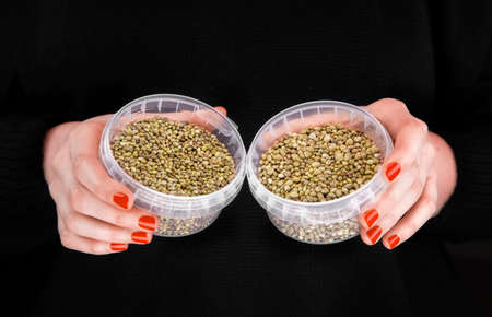Two plastic jars with hemps in woman's hands in a black backgroundの写真素材