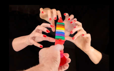 Man's hand giving a colorful pipe and four woman hands taking it in a black background