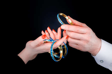 Men's hand giving blue bracelet to woman's hands in a black backgroundの写真素材