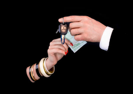 Men's hand giving to  woman's hand euro banknotes and car keys  in a black background