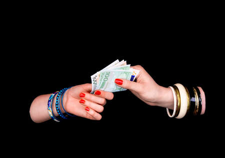 Female's hand giving to other  woman's hand euro banknotes in a black backgroundの写真素材