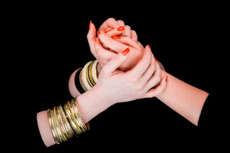 Two women's hands with bracelets holding each other in a black backgroundの写真素材