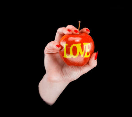 Woman's hand with an apple with word love on it in a black backgroundの写真素材