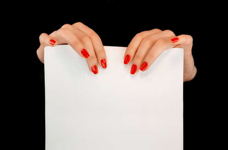 Woman's hands with red nails holding a white sheet of paper in a black backgroundの写真素材