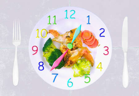 Clock made of a stew plate with chicken wings and vegetables, fork and knifeの写真素材