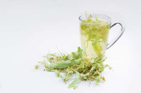 Cup of linden flower tea with blossoms inside on a white background