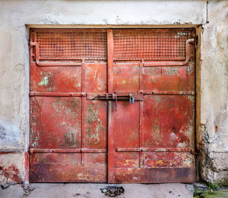 Metal padlock on a red metal old garage gates with handle in an old houseの写真素材