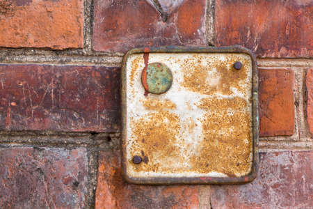 Close view of an old metallic red rusty plate on a brick wall