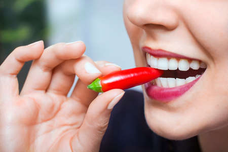 Natural sexy caucasian  woman with red hot chili pepper in mouth in a blurry backgroundの写真素材