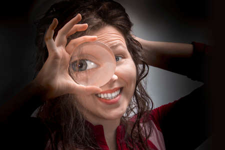 Female  eye looking through magnifying glass close up, in a black backgroundの写真素材