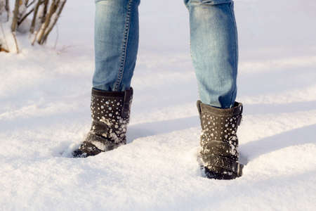 Woman's legs with blue jeans and black shoes in a white snow