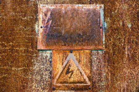 Old rusty tin surface with warning sign of high voltage for backgroundの写真素材