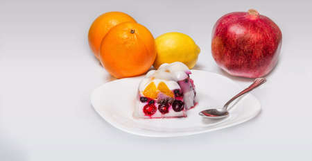Close view of a colorful jelly cake with a variety of fruits in a  white plate and orange, pomegranate and lemonの写真素材
