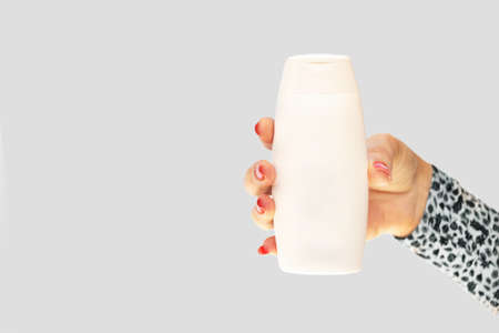 Female's hand with red nails holding a white plastic bottle on a grey backgroundの写真素材