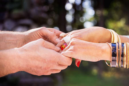 Male's hands holding female's hands with red nails, rings, and golden braceletsの写真素材