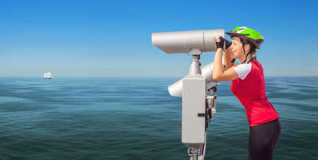 Young sporty cyclist woman watching to the sea through a telescopeの写真素材