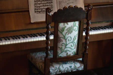 Old vintage chair near a wooden piano and a sheet paper on itの写真素材