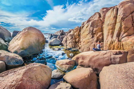Woman sat in meditation pose on the stone in a rocky Norwegian coastの写真素材
