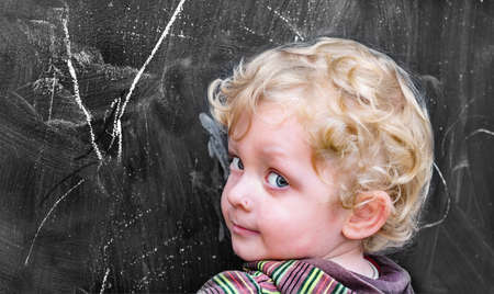Little boy with curly hair at the old black school boardの写真素材