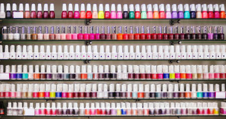 Many colorful small nail polish bottles on glass shelves
