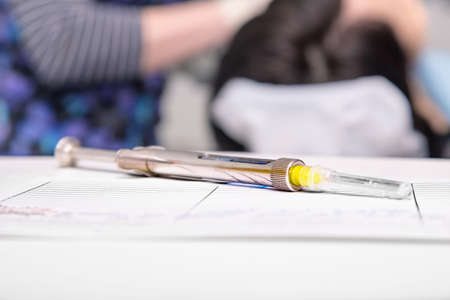 Surgical steel dental syringe with anesthetic cartridge on a white dentist tableの写真素材