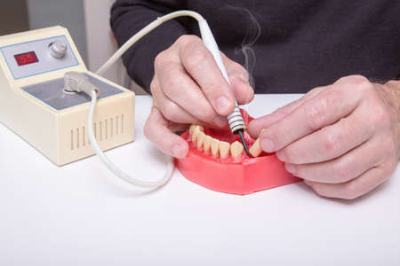 Close up of menâs hands working with electric waxer on a red wax dental model on a white tableの写真素材