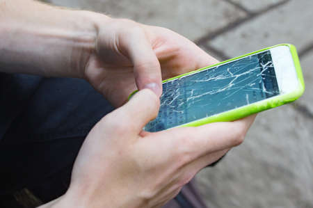 Close view of man's hands with a greenmobile phone whose screen is crackedの写真素材