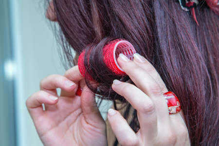 Womanâs hands with red rings and red curler in hair. Close up.の写真素材