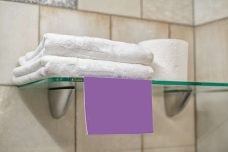 Two white towels, a roll of toilet paper and a blank lilac label on the glass shelf in the bathroom. close up.の写真素材