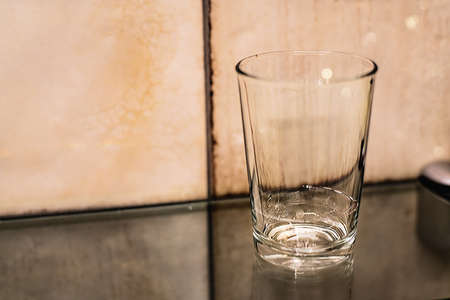 A litte bit of water in a glass standing on a glass shelf in tiles background. Close up.の写真素材