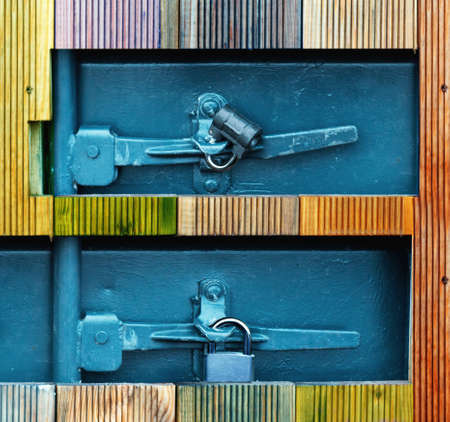 Square holes in a wooden wall with two small padlocks on a grey metallic door. Close up.の写真素材