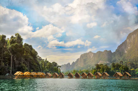 Landscape with small wooden buildings on the water, covered with reeds. Cloudy sky. Thailand.