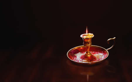 Finishing burning candle in an ancient brass candle holder on a warm dark backgroundの写真素材