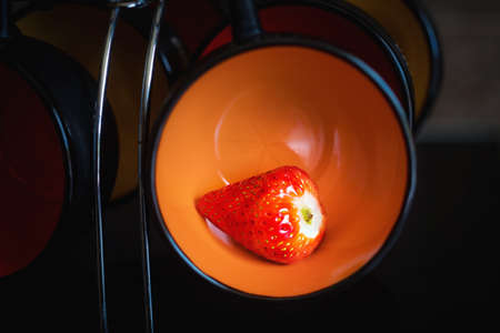 Ripe strawberry in an orange  cup on a cups holder  in a black background. Close up.の写真素材